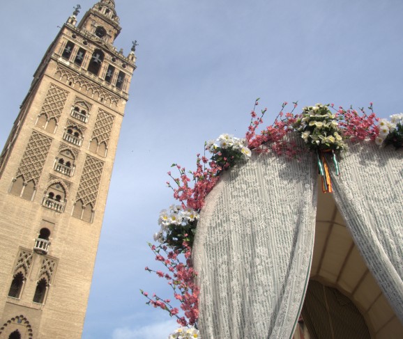 A flower-festooned wagon passes the Giralda in Seville.